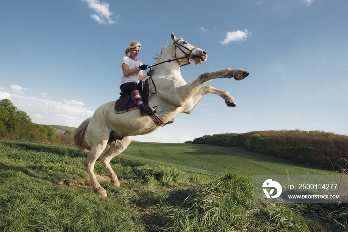 Young female rider, jumping  with white horse