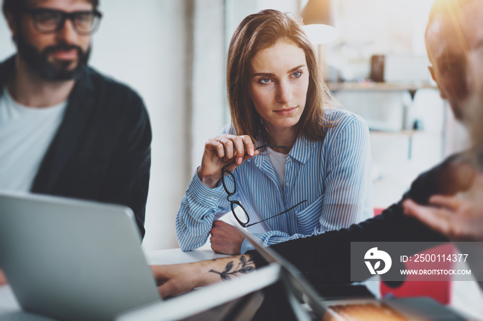 Three coworkers at working process.Young woman working together with colleague at modern office.Teamwork concept. Blurred background.Horizontal.