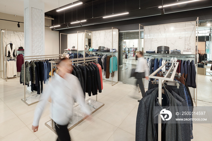 Blurred motion of sales consultants in clothing store with racks and accessories on shelves