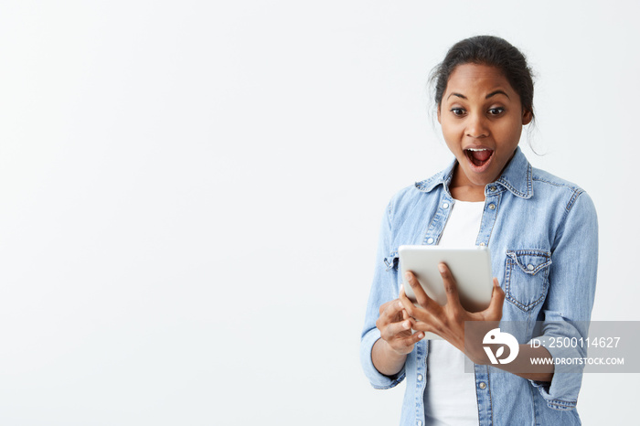 Portrait of excited young African American female screaming in shock and amazement holding new tablet in her hands. Surprised bug-eyed dark-skinned girl looking impressed, can’t believe her own eyes