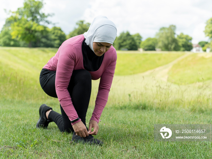 UK,Sutton,Woman in headscarf and sports clothing tying shoe in meadow