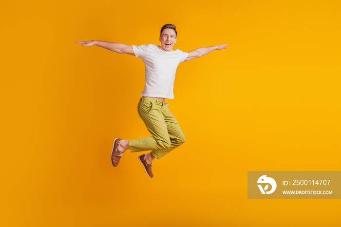 Portrait of athletic energetic active guy jump pretend airplane hands wings on yellow background