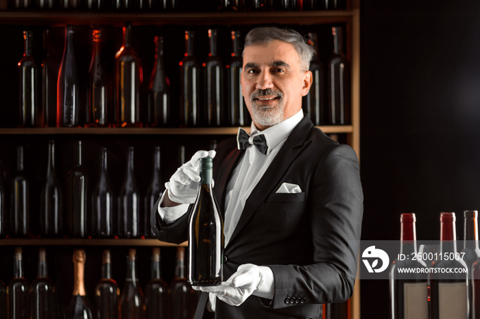 Elegant waiter sommelier wine steward with a bottle of wine. Examination of wine products. Restaurant staff among shelves of wine bottles. Stylish middle-aged man with a grey beard.