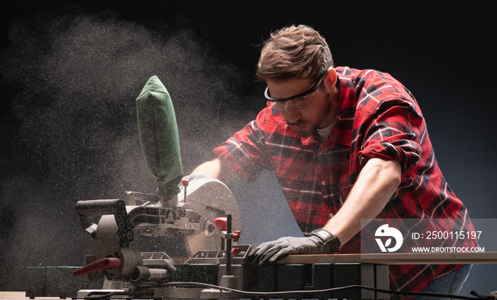 Handsome man using modern electric circular saw in the workshop