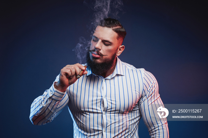 Handsome and elegance bodybuilder with beard and fashionable hairstyle smoking cigar in studio background.