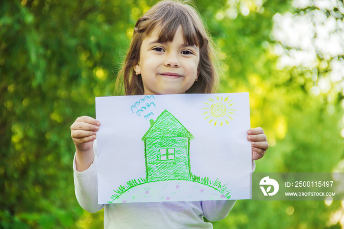 Drawing of a green house in the hands of a child. Selective focus.