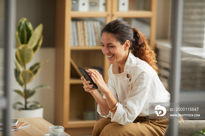 Portrait of elegant adult woman looking at smartphone screen and laughing while chatting online with friends and family, copy space