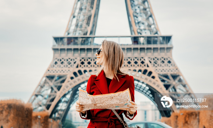 Style redhead girl in red coat and bag with map in parisian park in autumn season time. Eiffel tower on background