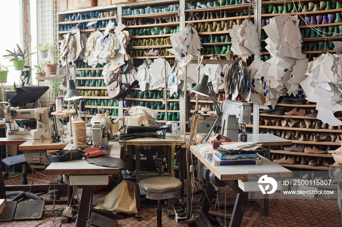 Image of workshop with tables with sewing machines on them shoe models and patterns on the shelves in the background at a shoe factory