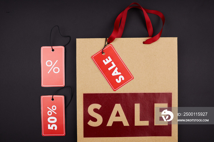 High angle view of tags for store sale and paper bag with red inscription on black background