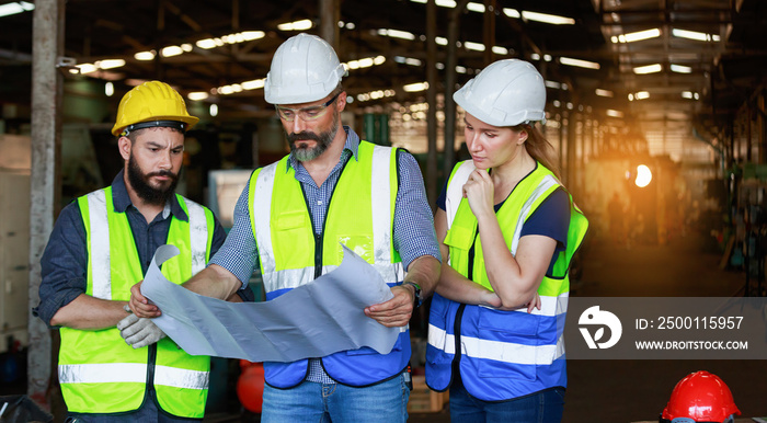 Male and female engineers chat with factory workers as they use machine drawings, planning for industrial maintenance