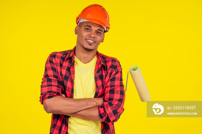 latin brazilian cleaning man wearing hardhat and painting the walls in studio yellow background