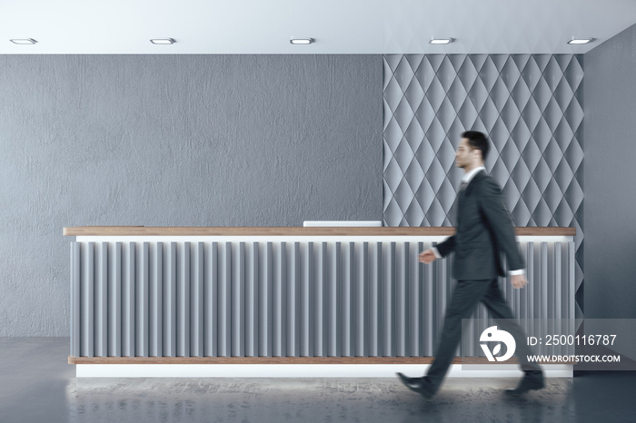 Businessman walking in hotel corridor with reception table.