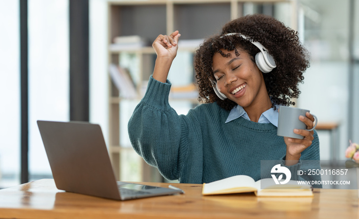 Happy african american businesswoman wearing headphones sitting and talking Listening to music in a relaxed manner and smiling happily at the office.