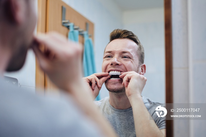 Young man preparing silicon tray for teeth whitening with bleaching gel. Themes dental health, care and beauty.