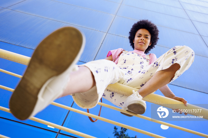 Black woman sitting on fence near building