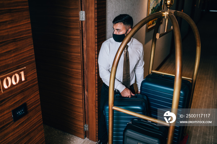 Bellboy with luggage cart in hotel hallway. He is  bringing luggage to guest rooms.