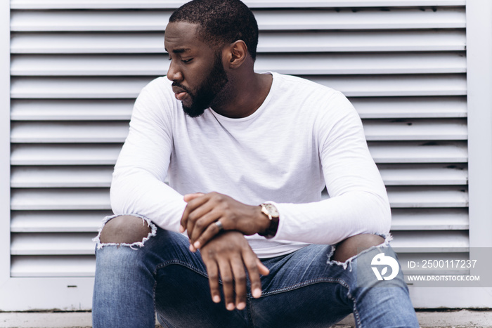 Handsome Afro American man wearing casual clothes in modern city sits near the building