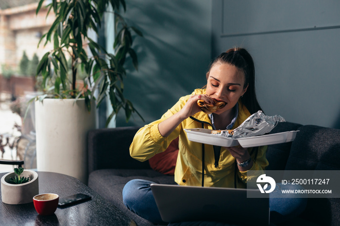 woman eating lunch while sitting on sofa and using laptop computer at her home