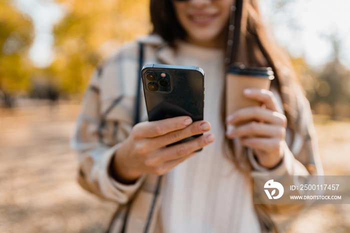 close-up hands holding phone of young woman walking in autumn park using app on smartphone