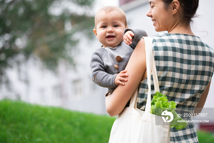 Young mother with baby son walking and shopping fruits and vegetables with reusable cotton Eco produce bag. Zero waste lifestyle concept. Concern for the next generation