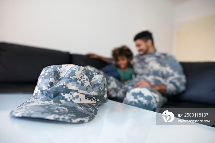 Military leave and service. Close up view of military camouflage hat or cap while in background off-duty soldier in uniform enjoying reunited happy family moments.