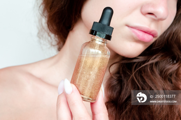 young beautiful curly woman uses gold serum for face on white background. The concept of facial skin care.