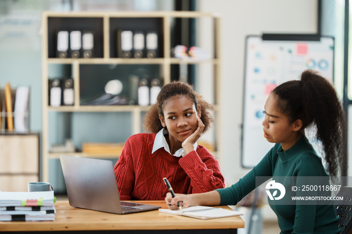 Focused young african american businesswoman or student looking at laptop holding book learning, serious black woman working or studying with computer doing research or preparing for exam online