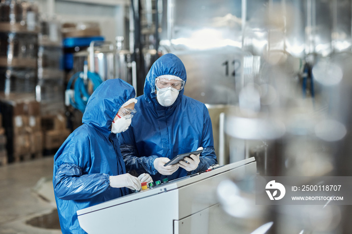 Two workers wearing protective gear operating equipment at industrial factory