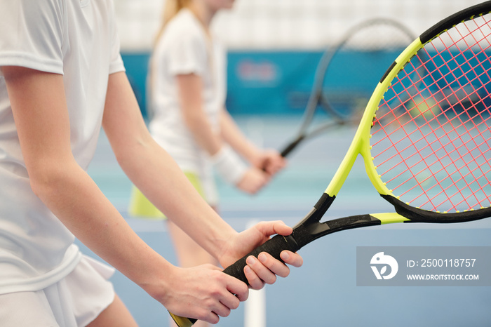 Hands of active teenage girl standing on stadium and holding tennis racket