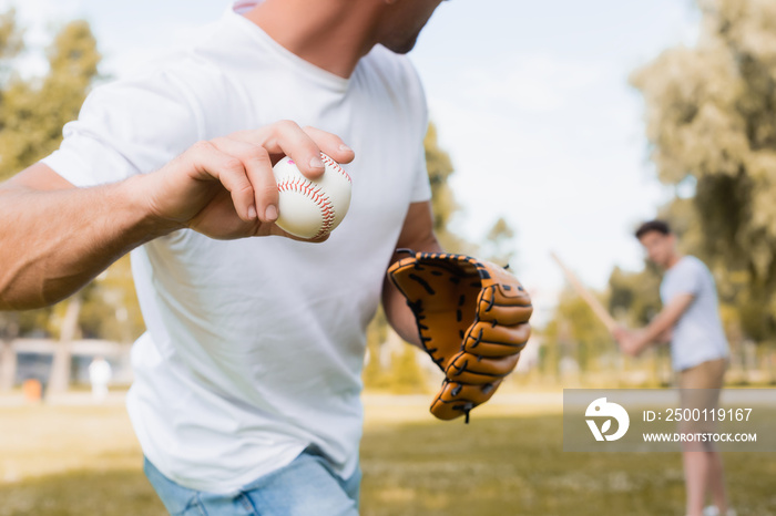 cropped view of man in leather glove playing baseball with teenager son in park