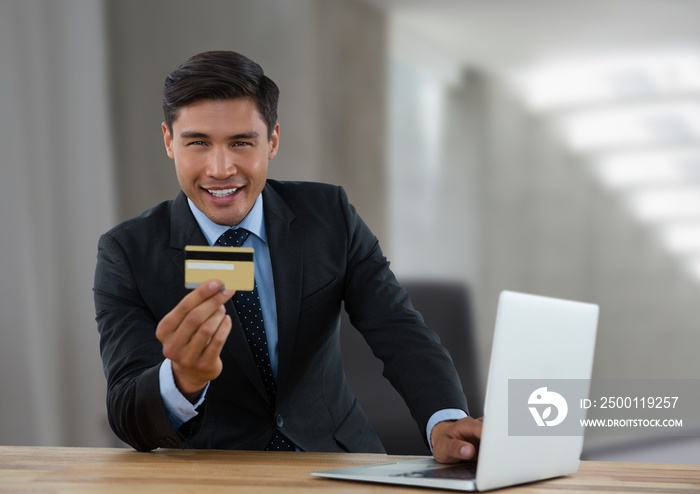 Portrait of asian businessman with laptop holding a credit card against office in background