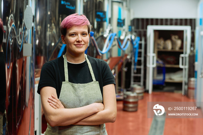 Young female worker of beer production factory in apron crossing arms by chest