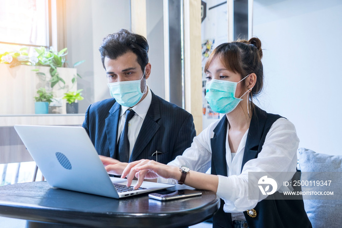 sian female and Businessman workers meeting together with laptop and wear protective masks prevent PM 2.5 and corona viruus or covic19 at co working space .Health and teamwork concept