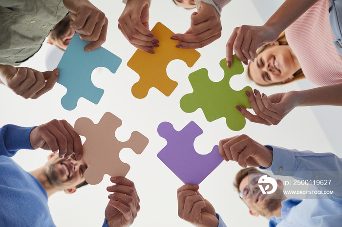 Young business people hold puzzles as symbol of cooperation, problem solving, thinking about creative ideas, brainstorming and teamwork. Bottom view of smiling people holding colored pieces of puzzles