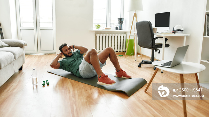 Your personal trainer. Male fitness instructor showing exercises while streaming, broadcasting video lesson on training at home using laptop. Sport, online gym concept