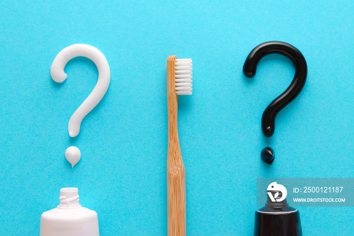 question from white and black toothpaste, teeth care concept, wooden toothbrush on blue background