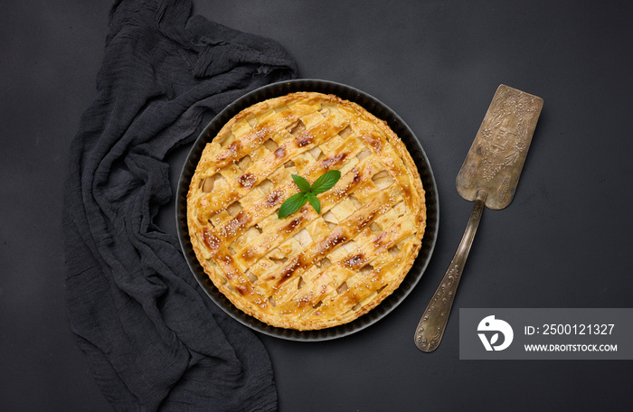 Round baked apple pie on a black table. View from above