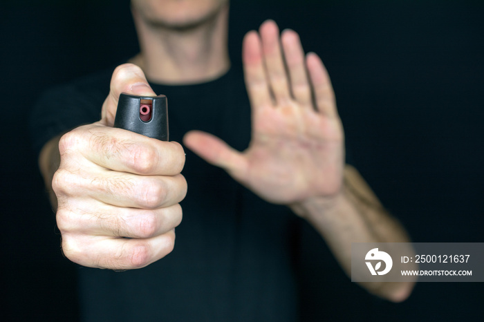 pepper gas in the hand of a young man in a black jacket CS spray self-defense Tear gas concept, close up, selective focus , blurred dark background