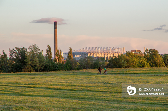 Friends cycle through Newcastle-Upon-Tyne’s Town Moor park with the impressive structure of St James Park football stadium looming large in the background