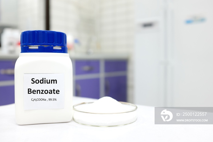 Selective focus of bottle of pure sodium benzoate food additive beside a petri dish with white solid powder substance. White laboratory background with copy space.