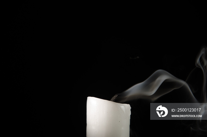 Burning candle with fading flame and smoke on a black background