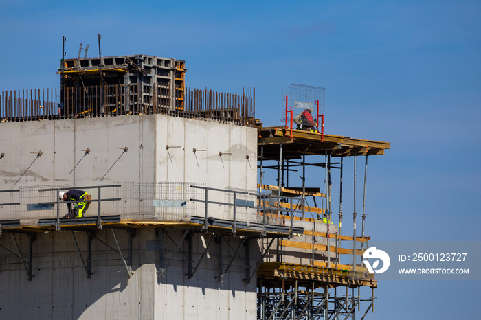 Workers working at height on the construction of a public facility. Collection of structural elements from the construction crane sling. Photo taken on a sunny day. Grodzisk Mazowiecki, Poland