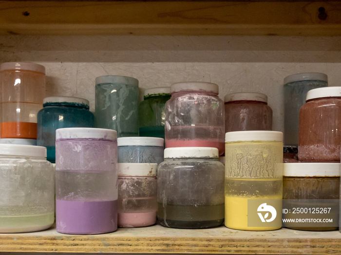 Jars of coloured pottery glaze on wooden shelf in studio