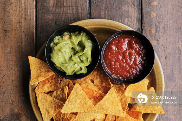 Nachos chips with salsa and Guacamole sauce on a brown plate on a wooden background, top view. Mexican food. Mexican cuisine