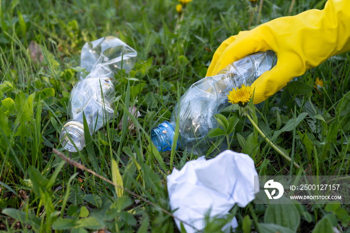 A volunteer removes garbage in the Park. A woman’s hand in a yellow rubber glove lifts a plastic bottle