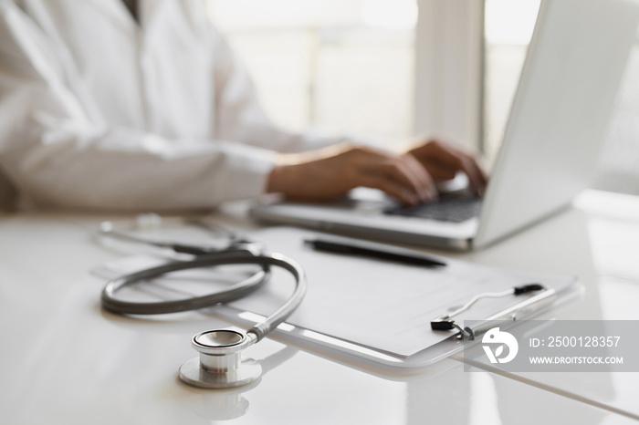 Doctor medical professional working on laptop, focus on stethoscope. Physician, therapist or practitioner filling medical documents, writing prescription for patient. Health care, medicine concept