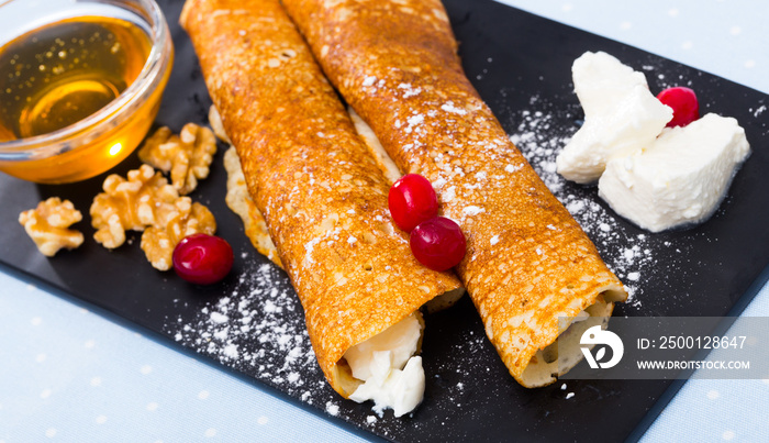 Bulgarian-style crepes Palatschinke with filling of soft cheese and walnuts with honey on black board