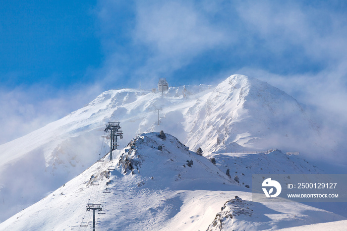 Empty ski lift heading toward the top of the snow-capped mountain lost in the cloud.