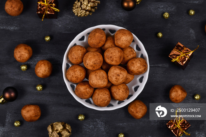 Traditional German Christmas sweets called ’Marzipankartoffeln’. Round ball shaped almond paste pieces covered in cinnamon and cocoa powder in white bowl on dark background